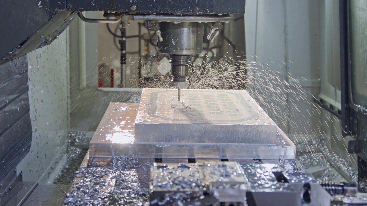 CNC machine cutting a steel mold cavity with coolant and metal chips flying