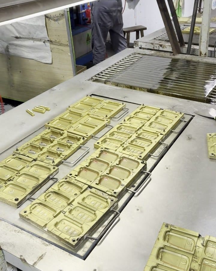 Brass multi-cavity silicone mold plates laid out on a workbench, each plate holding many cavities